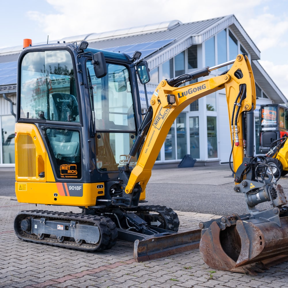 Gelber LiuGong 9018F Minibagger mit Schaufel, vor einem Gebäude mit Solarpaneelen.