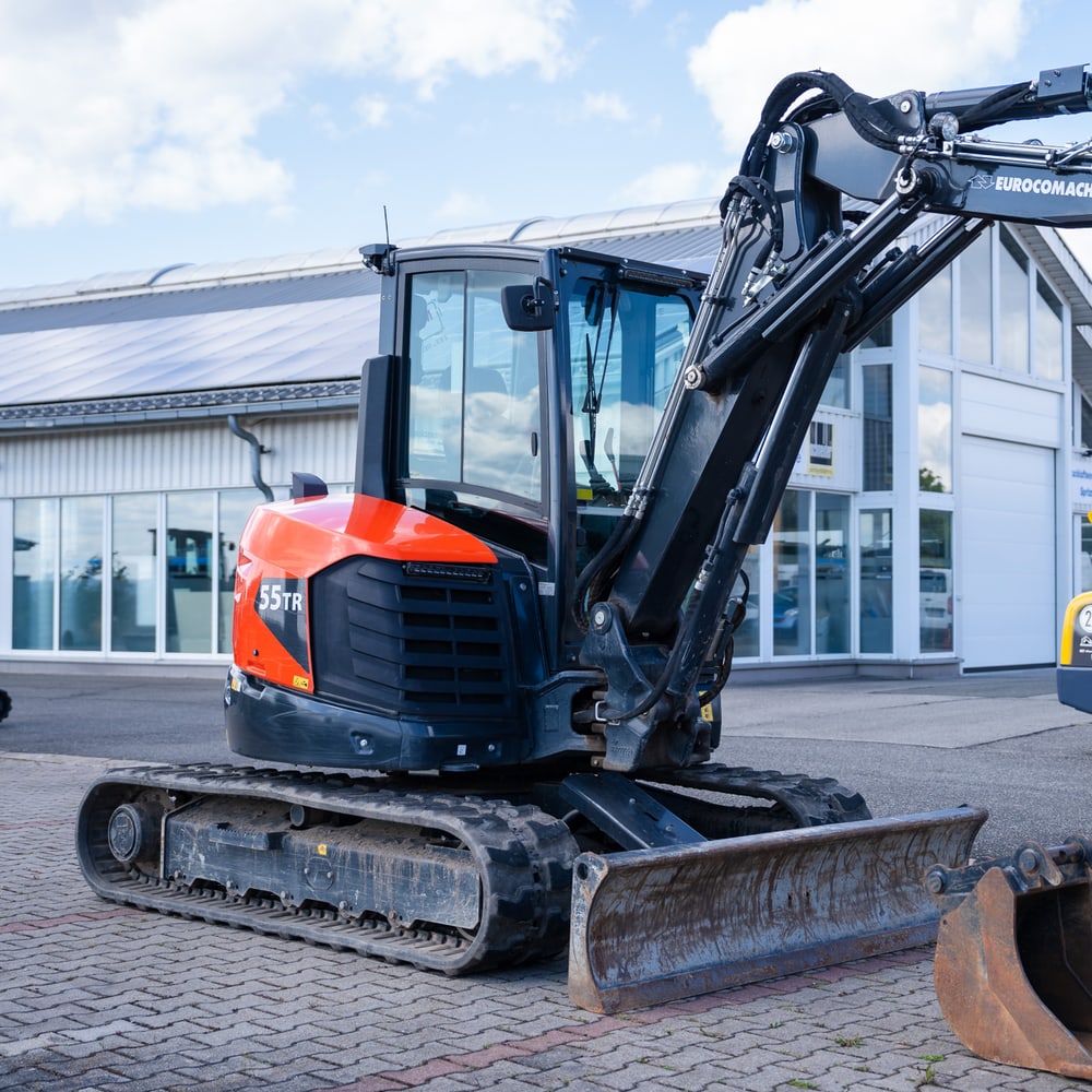 Ein oranger und schwarzer Kubota 55TR Minibagger steht auf einem gepflasterten Hof vor einem Gebäude.