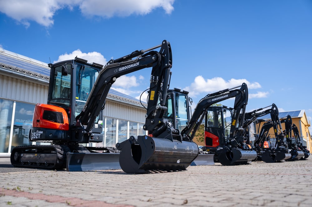 Vier orange-schwarze Doosan Minibagger stehen auf einem gepflasterten Hof unter blauem Himmel.